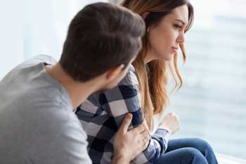 Man supporting a distressed woman while they look out a window.