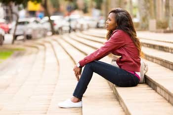 Woman in a red top sitting alone outdoors while considering abortion procedures in Spanish.