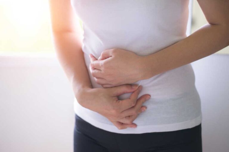 Woman holding her stomach in discomfort while standing indoors.