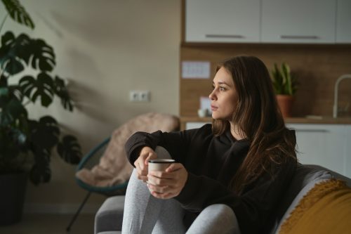young woman sitting on her couch with a cup of coffee thinking